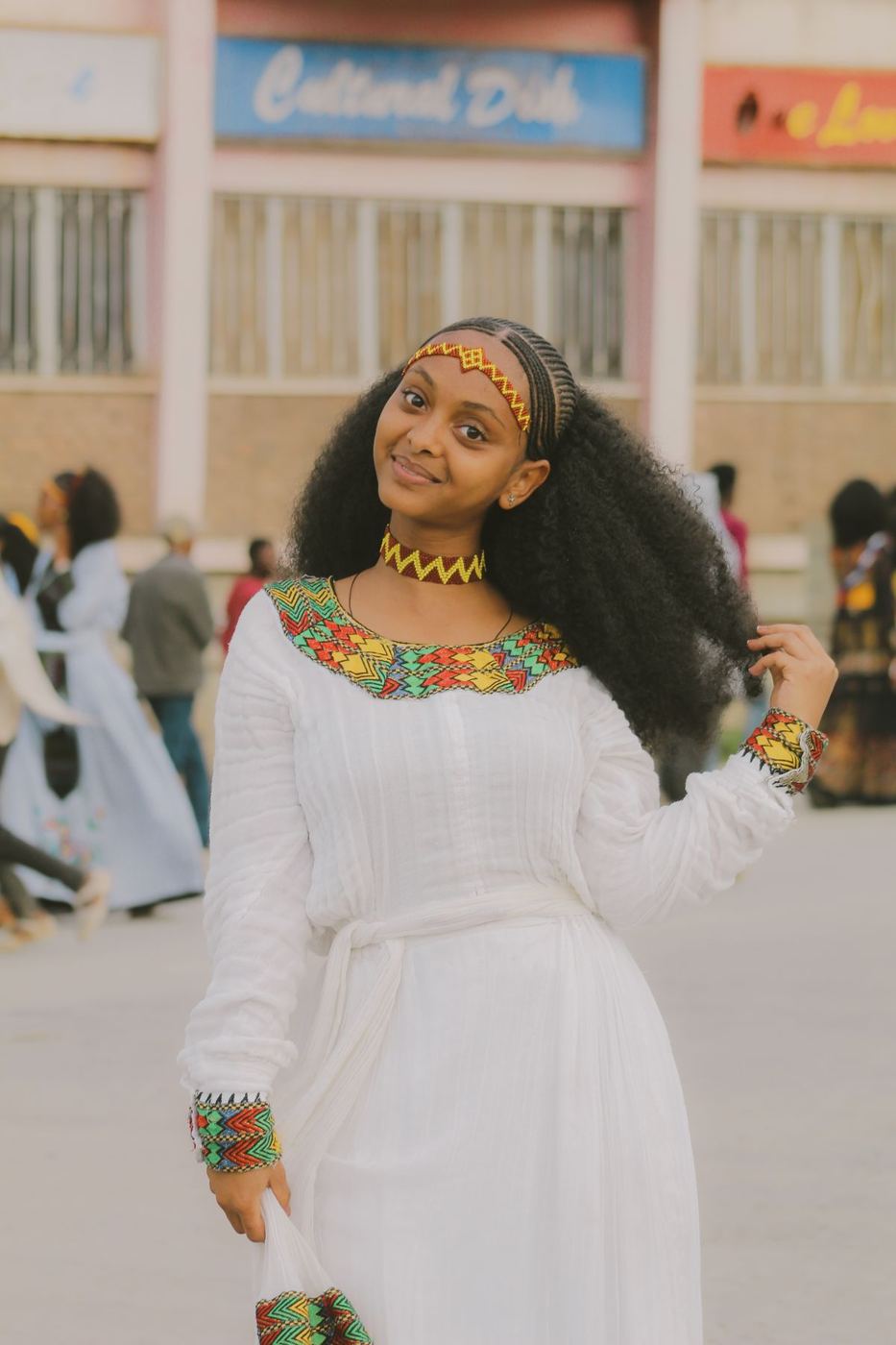Woman smiling in a white habesha dress with colourful tibeb embroidery